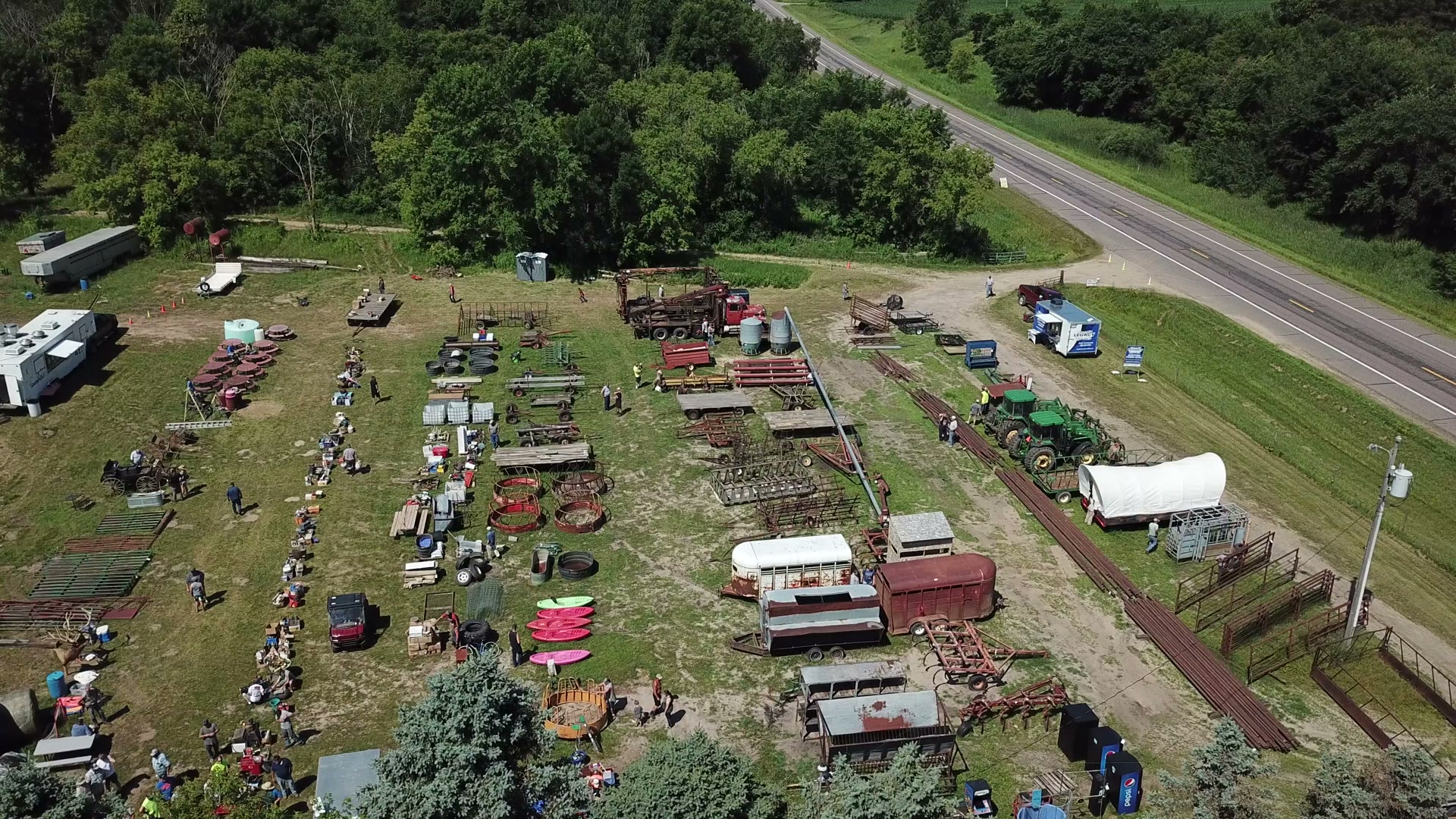 Aerial drone photo of a Central Minnesota estate auction with equipment rows, tractors, and buyers