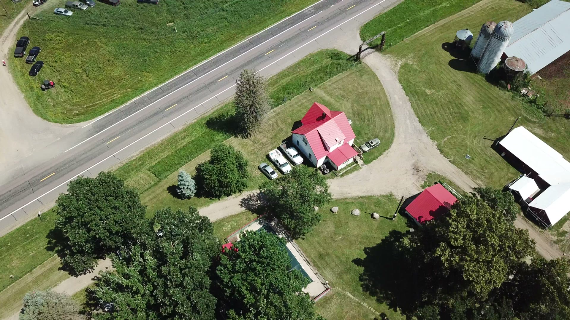 Top-down drone photo of a Minnesota farmstead with red metal roofs, silos, and highway frontage