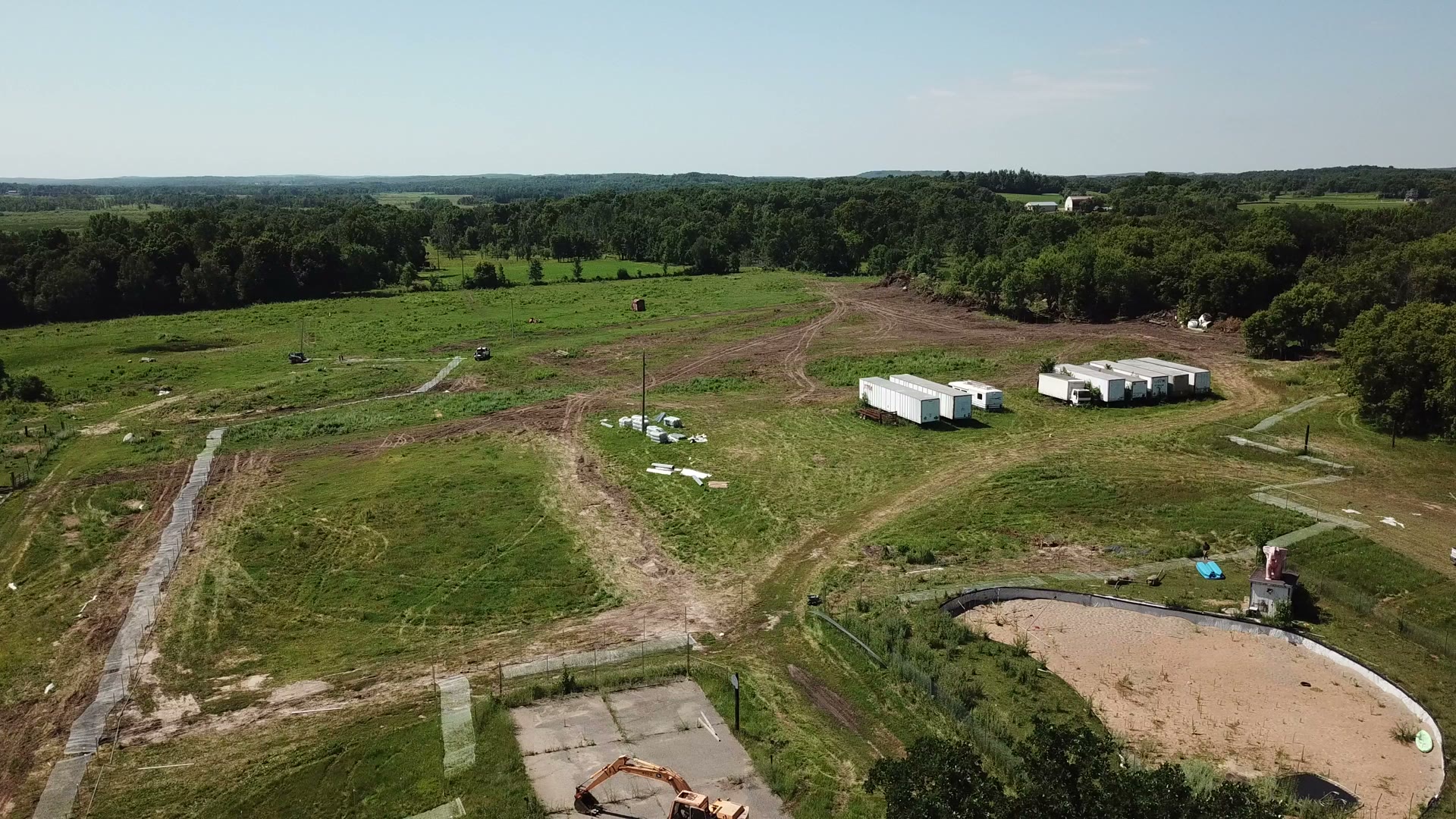 Drone overview of rural Minnesota property with outbuildings, trailers, and treeline